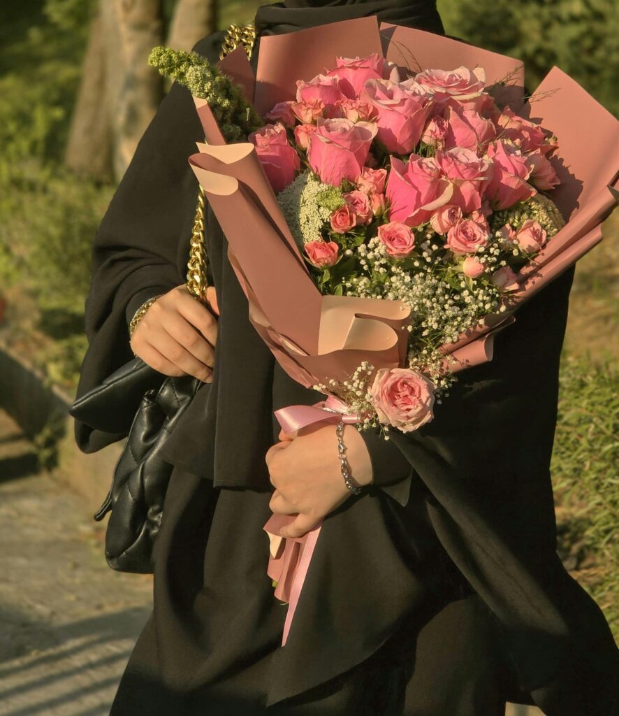 A woman in black attire holds a beautiful bouquet of pink roses outdoors.